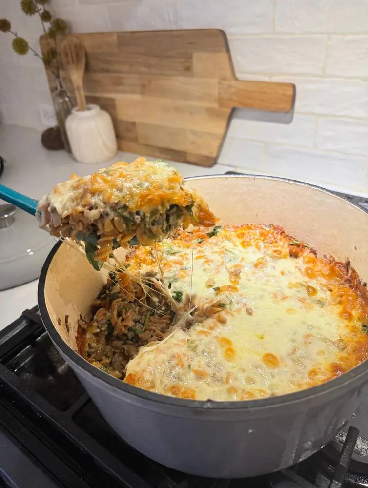 High-protein Philly cheesesteak pasta bake with a melted provolone cheese pull, made with lean ground beef and fusilli in a Dutch oven