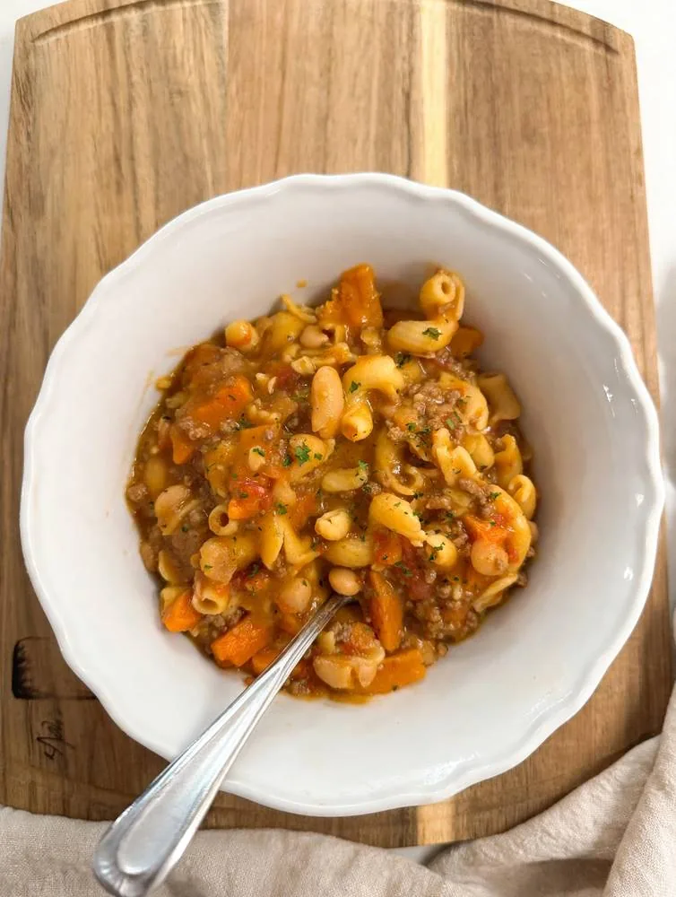 Bowl of high-protein Italian beef, bean and veggie soup with pasta, photographed overhead on a wood board